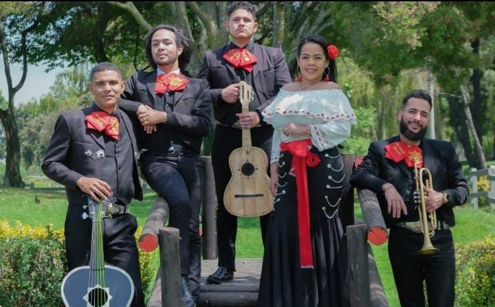Los cinco integrantes de Mariachi Estrella Mexicana con traje de charro negro y moño rojo en un parque de Bogotá